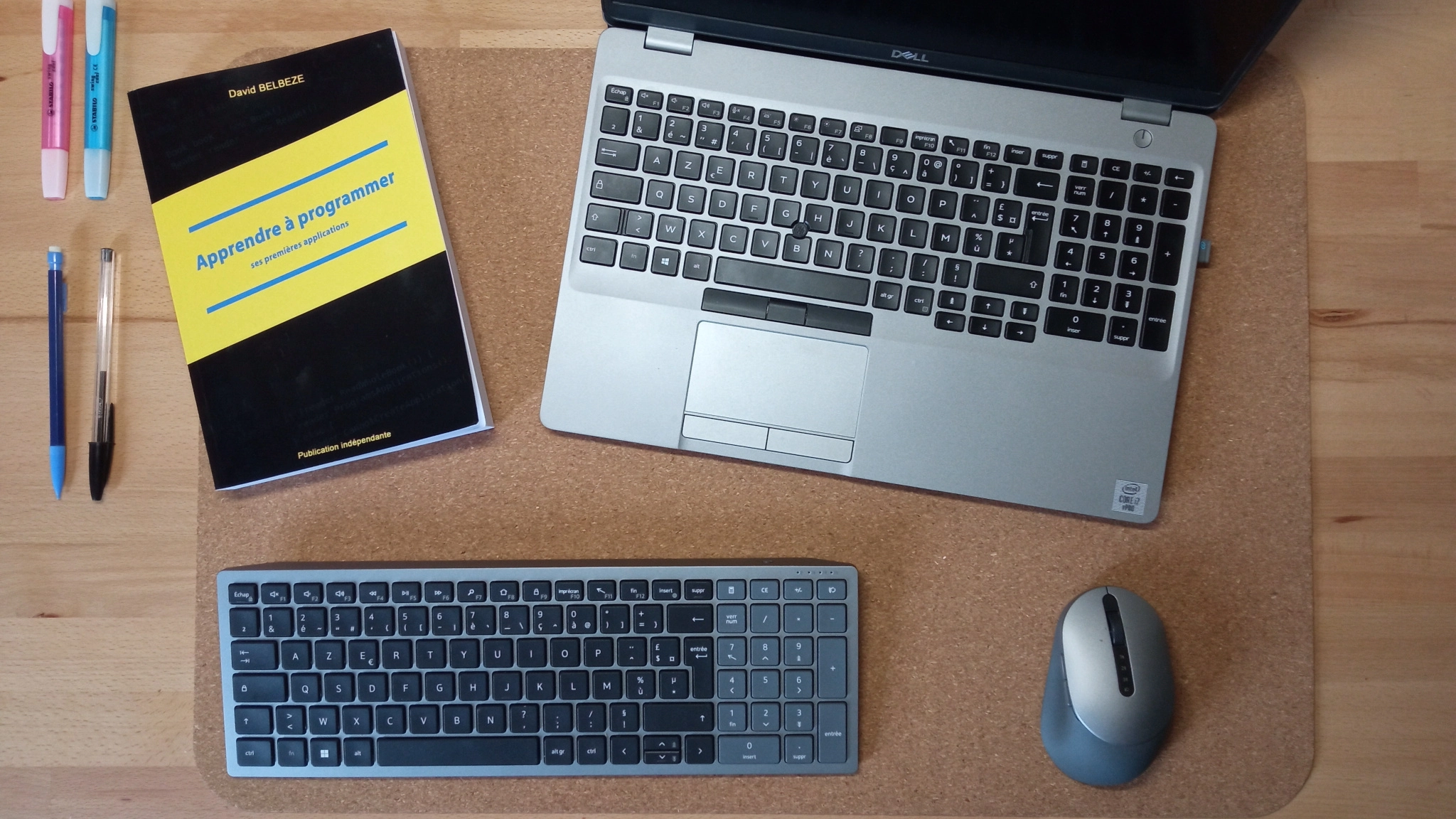 Un bureau de travail moderne avec un PC portable ouvert, accompagné d'une souris et d'un clavier sans fil. A côté, le livre \